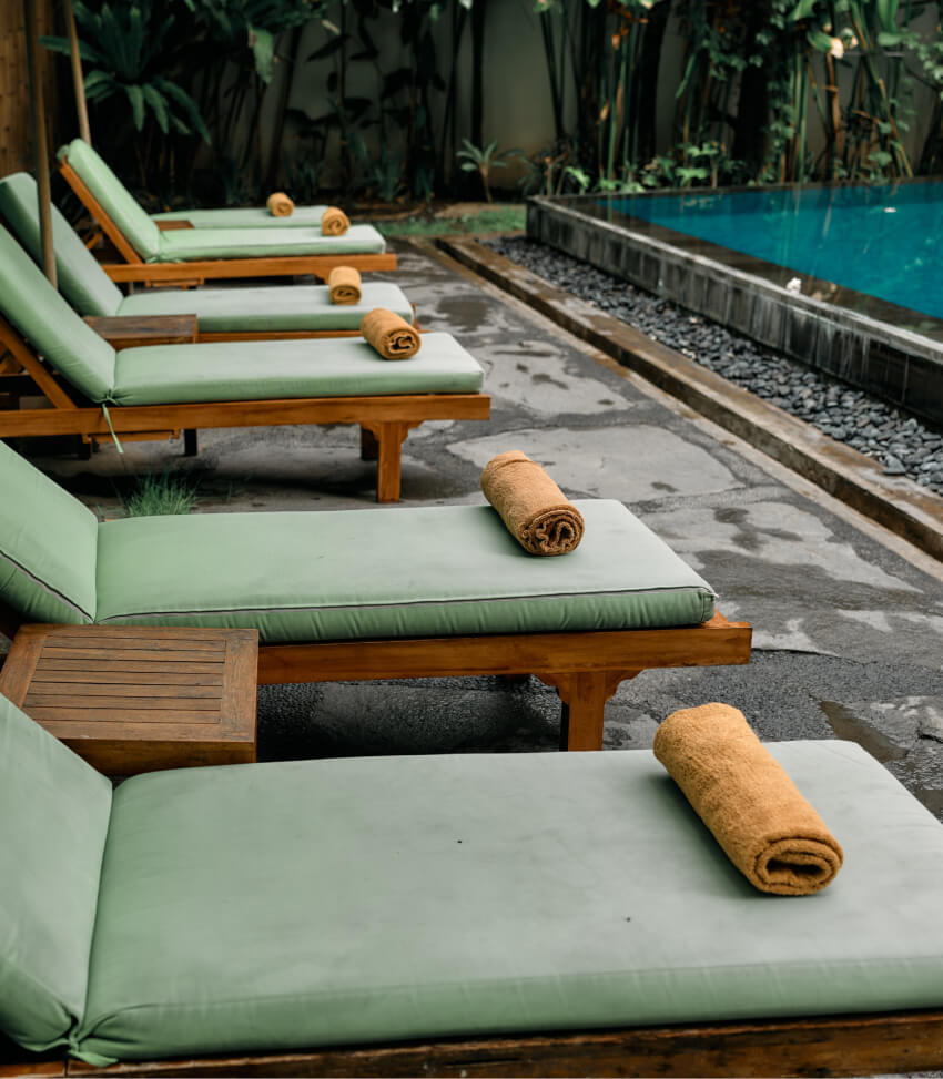 Resort poolside lounge chairs with rolled towels beside a calm pool surrounded by tropical greenery