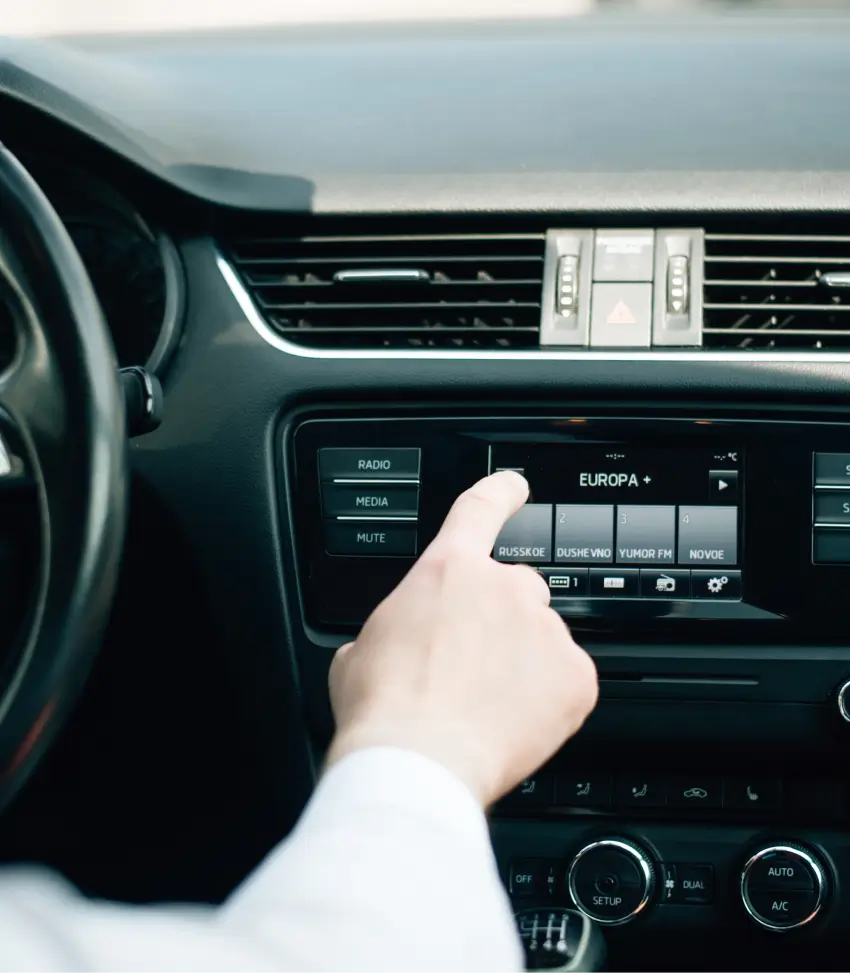 Person adjusting car radio to select a music streaming station on the dashboard display